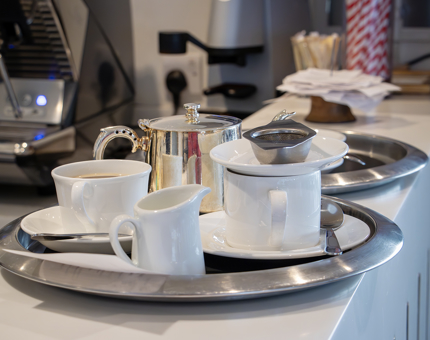 A tray containing a silver teapot, teacups and saucers and a jug of milk. 