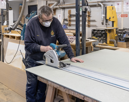A man using a cutting machine in the workshop to make a wooden till podium for the Royal Deck Tearoom.