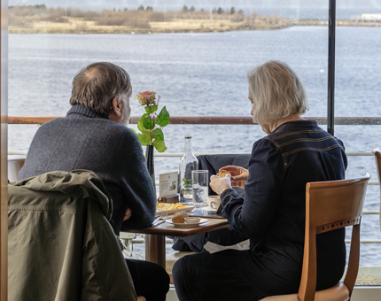 A couple sitting at a table in the Royal Deck Tearoom eating lunch. Views of water are in the background. 
