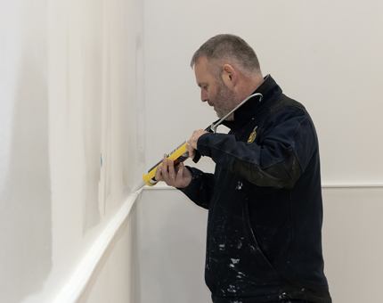 A man using a tube of sealant on a wall panel.