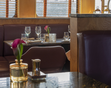 The inside of The Lighthouse Restaurant & Bar with tables set for dining. The chairs are purple leather and tables are grey marble. 