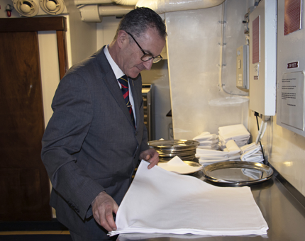 A man wearing a suit folding a white linen napkin. 