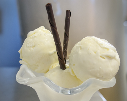 A glass dish containing scoops of vanilla ice cream and chocolate straws.