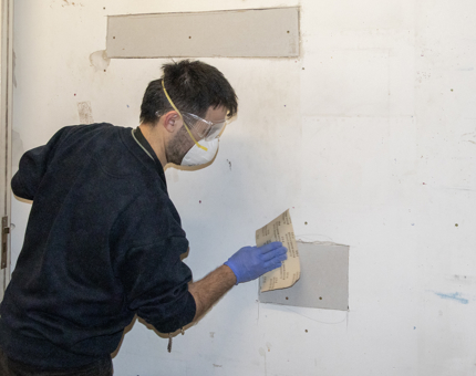 A member of the Maintenance team sanding a wall in preparation before painting.
