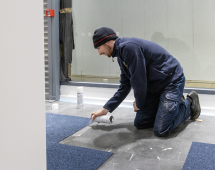 A member of the team laying carpet floor tiles in the new temporary Ticket Office.