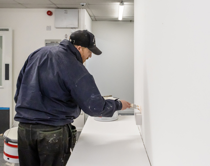 A man from Maintenance painting a wall in the temporary Ticket Office. 