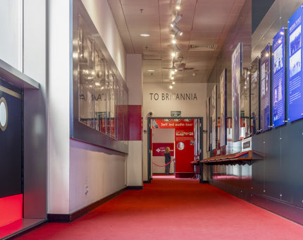 The red carpet in the Visitor Centre leading to the bridge walkway. There are photographs and display panels on the wall. 