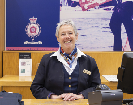 A woman in Britannia uniform smiling behind the Gift Shop till. 
