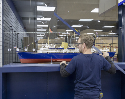 A member of the Maintenance team disassembles the glass cabinet which displays the LEGO replica model of Britannia. 
