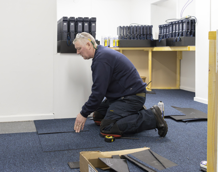 A member of the Facilities team laying blue carpet tiles on the floor in the temporary Ticket Office.