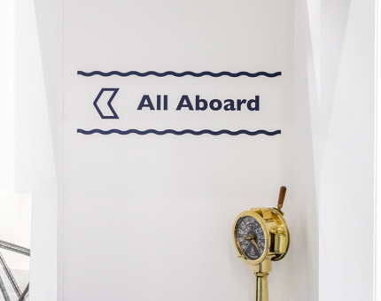 Blue and white signage 'All aboard' on the wall and a brass engine order telegraph.