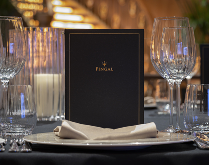 A table setting in Fingal's Ballroom with a menu, glasses and linen napkin.