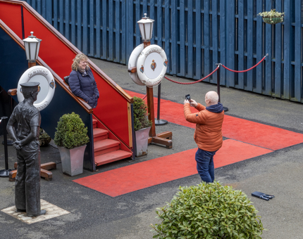 Visitors pose and take a photo on the Royal Brow. A red carpet is next to the Royal Brow and there are ceremonial perrybuoys either side. 
