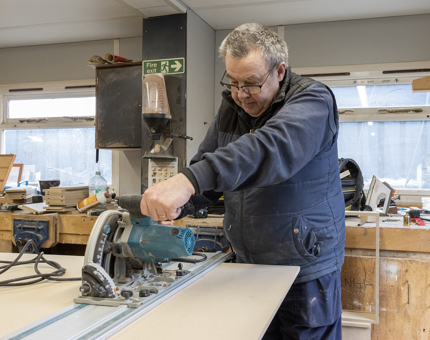 A man from the Maintenance Team using a cutter for wood in the workshop.