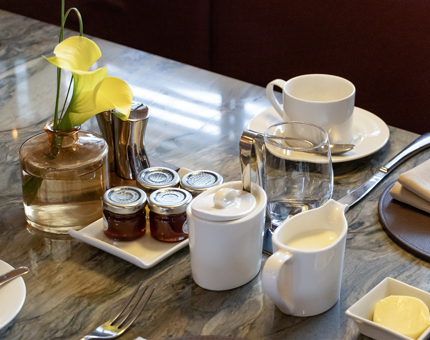 A table setting in The Lighthouse Restaurant & Bar for breakfast. There are miniature pots of jam on the table, a cup and saucer and a vase containing a flower. 