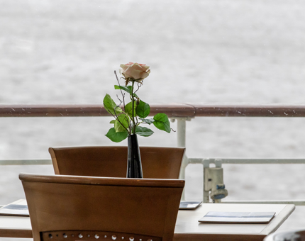 A table and chairs in the Royal Deck Tearoom. A view of water is in the background.