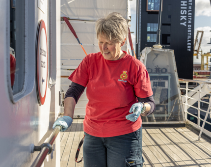 A female member of the Housekeeping team polishing a brass handrail on the Bridge. 