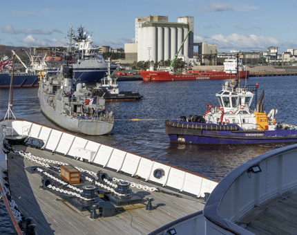 The bow of Britannia with a frigate, tug boat and other ships in the background. 