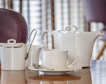A table set for tea with a teapot, milk jug, sugar jar, cup and saucer.