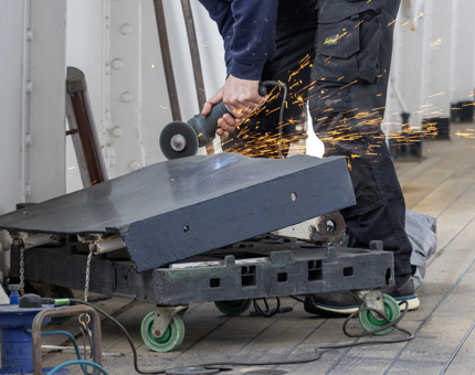 A man from the Maintenance team using a grinder on a gate.