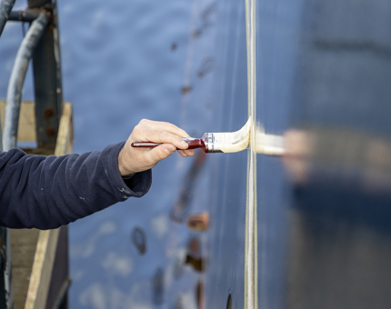 A man from Maintenance is painting on primer to the exterior of the ship. 