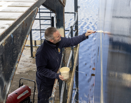 A man painting on primer before the gold leaf is applied.