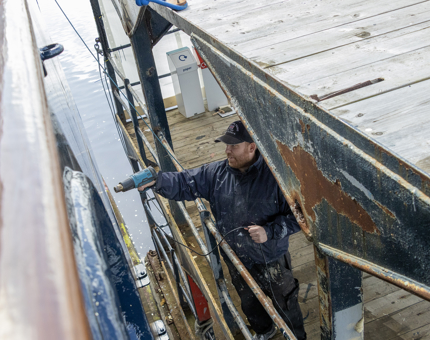 A man using a dryer on the filler on the ship's hull.