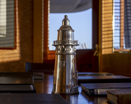 A silver wine cooler shaped like a lighthouse on the table in Fingal's Bridge. There are leather-bound log books on the table.