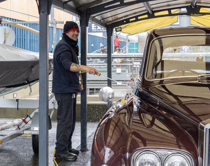 A member of the Facilities team hosing the Rolls-Royce car which is in the garage on the Quayside.