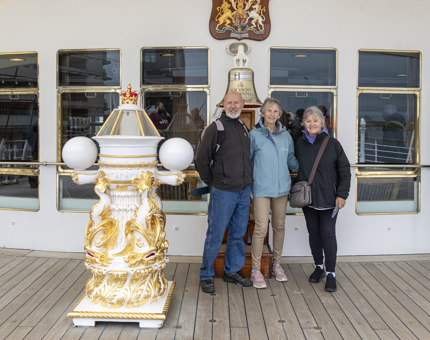 A man and two women stand posing for a photo next to the Bell and compass Binnacle.