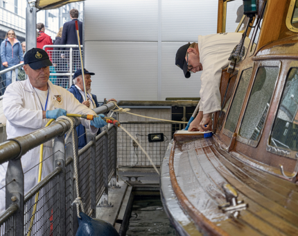 Three Yotties cleaning the outside of the Royal Barge.