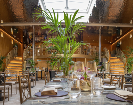 Downstairs in Fingal's Ballroom, tables are set for dining and large palm plants decorate the room. 
