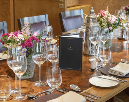 A close-up of a table setting in Fingal's Bridge. There are lots of different glasses on the table, floral arrangements, plates and cutlery. 