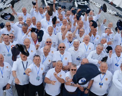 A large group of Yotties are standing in a group waving and throwing their caps in the air as they stand together on the Fo'c's'le Deck.