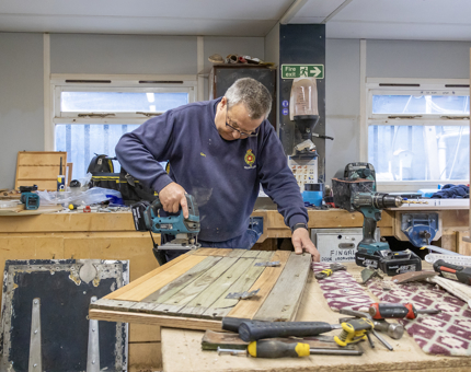 A man making a seat top for one of the whaler boats.