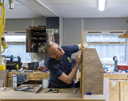 A man measuring up a length of wood for the new till point for the Tearoom.