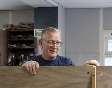 The man making the till point holding the wood and is smiling. 
