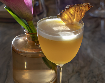 A mocktail next to a vase containing a lily.