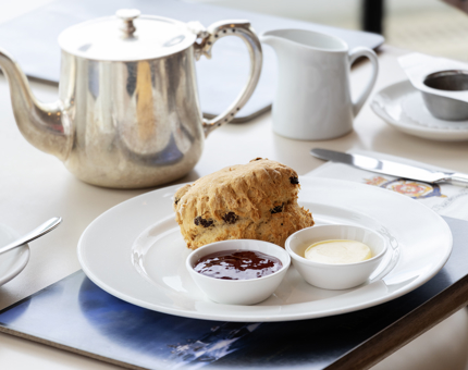 A table in the Royal Deck Tearoom containing a scone, jam, cream and a silver pot of tea.