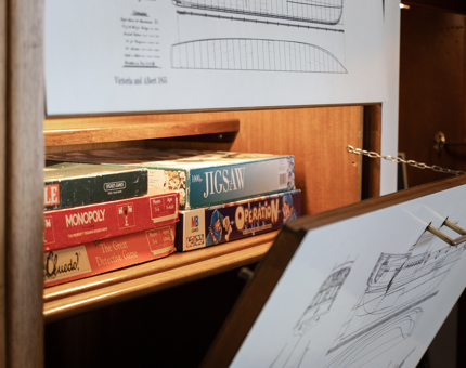 A concealed cupboard containing board games. The front of the cupboard has a ship illustration on the outside. 