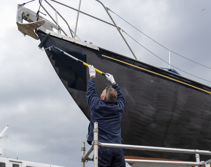 A member of the Maintenance team is holding a roller to paint the hull of Royal Racing Yacht Bloodhound.