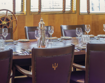 The Bridge dining space on Fingal. There are leather-backed chairs around a long table which is set for dinner with glasses and cutlery. 