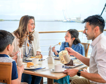 A family group of a woman and a man with a little boy and a little girl are enjoying cakes and tea sitting at a table in the Royal Deck Tearoom. 