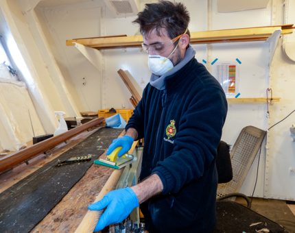 A man from Maintenance is sanding a barge pole. 