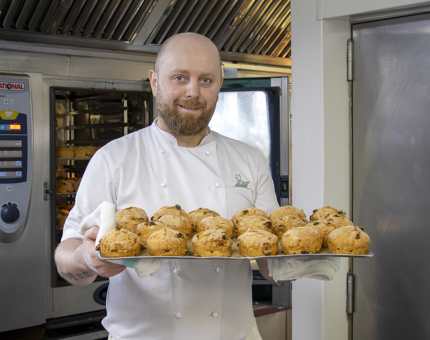 A chef taking a tray of scones out of the oven.