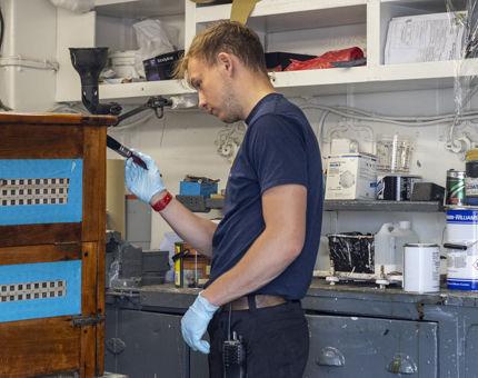 A man is varnishing a wooden rope box in the workshop.