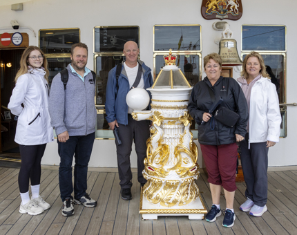 A group of visitors standing next to The Royal Yacht Britannia's Bell. 