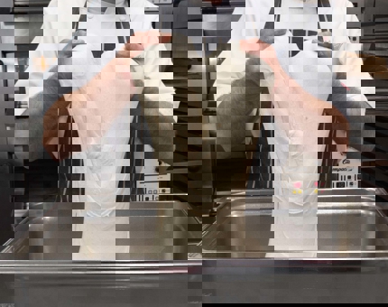 A Pastry Chef is stretching bread dough in the Galley. 