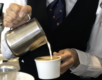 A Waiter is pouring a cappuccino. 