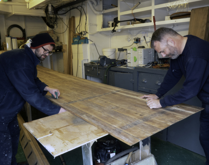 Two members of the Maintenance team are sanding in the workshop.